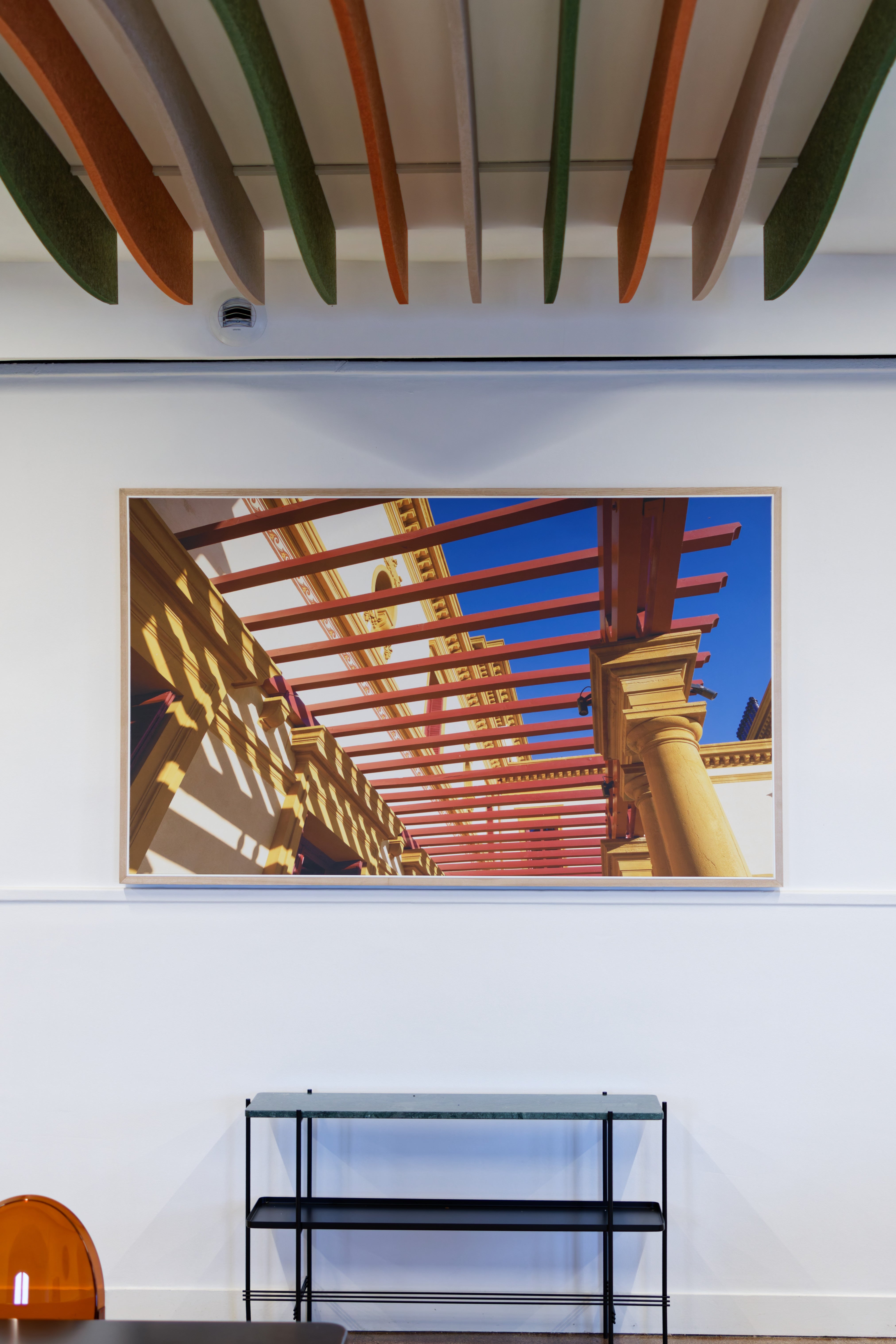 Deckenbaffel Wave Modular – Deckenbaffel – Farbige Pendelleuchte und modernes Regal in einem Büroumfeld mit Kunstwerk an der Wand.
