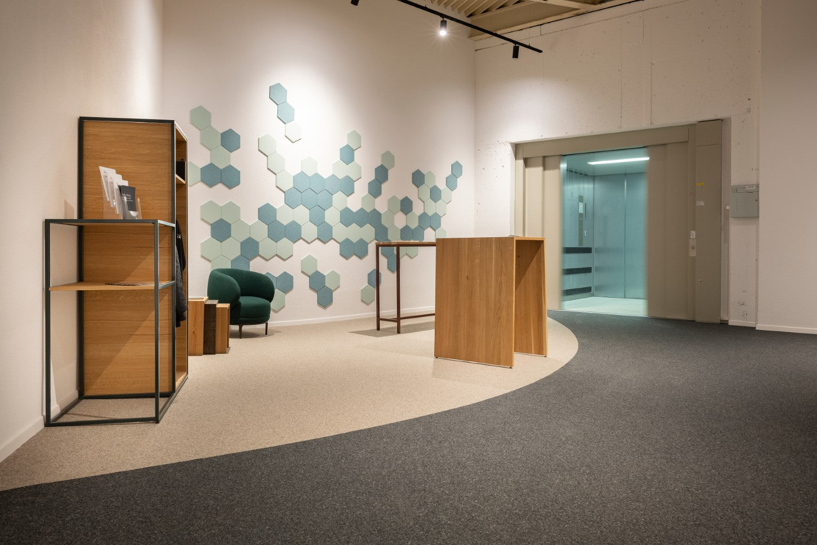 Wandverkleidung Hexagon – Akustische Wandverkleidung – Moderne Empfangsbereich mit hexagonalem Wanddesign, grüner Sitzgelegenheit und Holzmöbeln. Aufzug im Hintergrund.