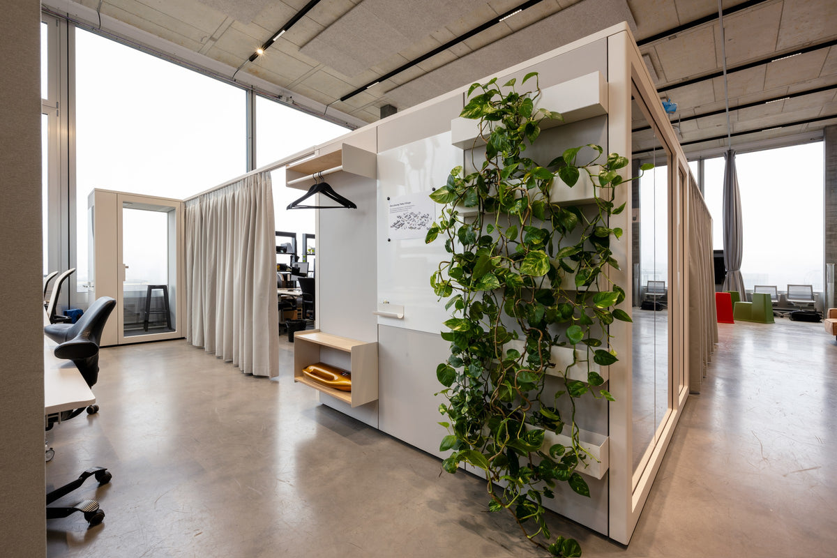 Talky Nook mit Pflanzenwand und Garderobe, aufgestellt in einer offenen Bürolandschaft.