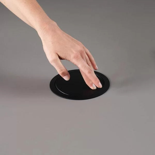 Konferenztisch | Parthos – Konferenztisch – Schwarze runde Abdeckung auf einer grauen Tischoberfläche, Hand greift nach der Abdeckung.