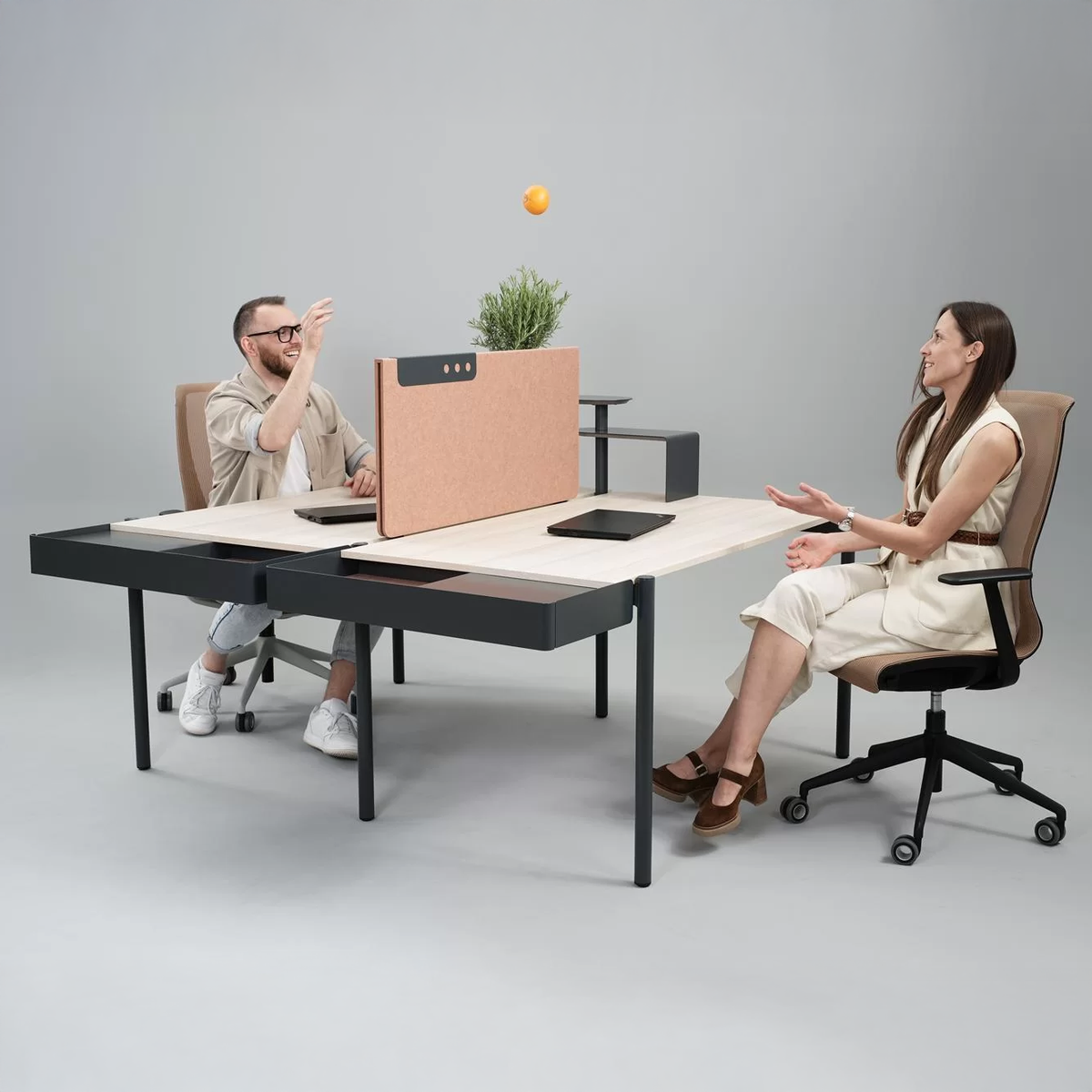 Zedo | Bench – Bench-Arbeitsplatzsystem – Zwei Personen an einem modernen Schreibtisch mit Trennwand und Pflanzen, interagierend, mit Laptops auf dem Tisch.