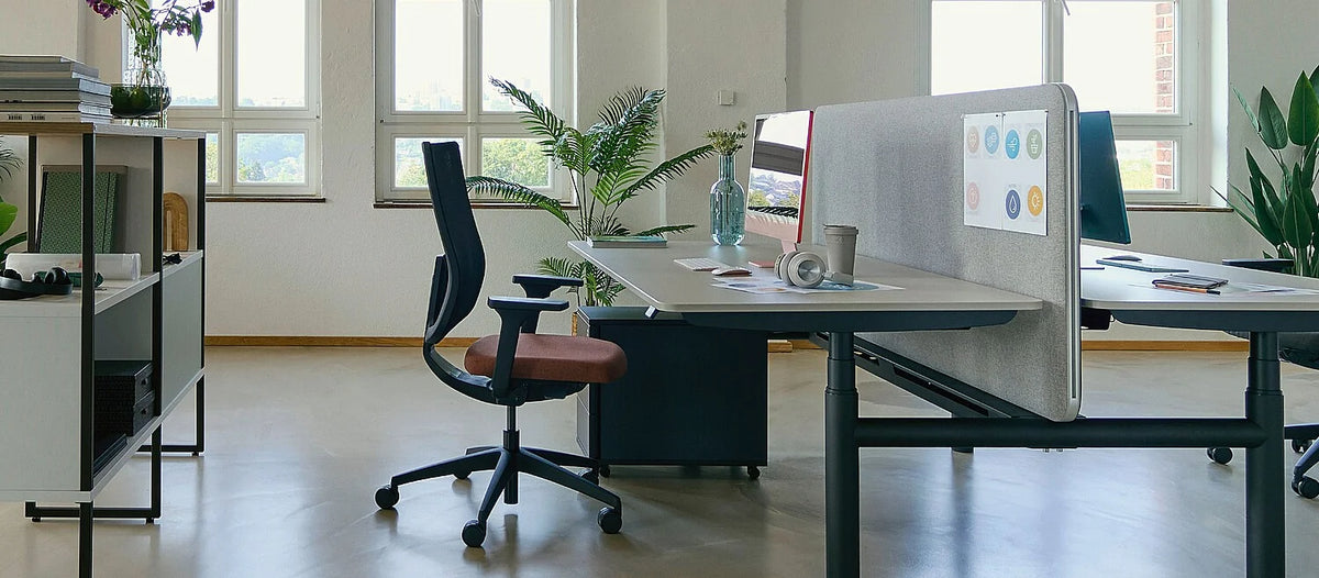se:do pro 2 – ergonomischer Bürostuhl – Moderner Schreibtisch mit grauer Oberfläche und schwarzem Gestell, Bürostuhl mit brauner Polsterung, Pflanzen im Hintergrund.