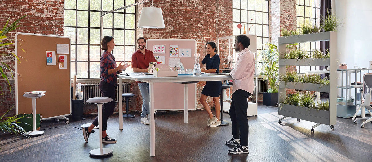 se:lab meet & stand – Besprechungstisch – Fünf Personen diskutieren an einem höhenverstellbaren Tisch in einem modernen Büro mit grossen Fenstern und Pflanzen.