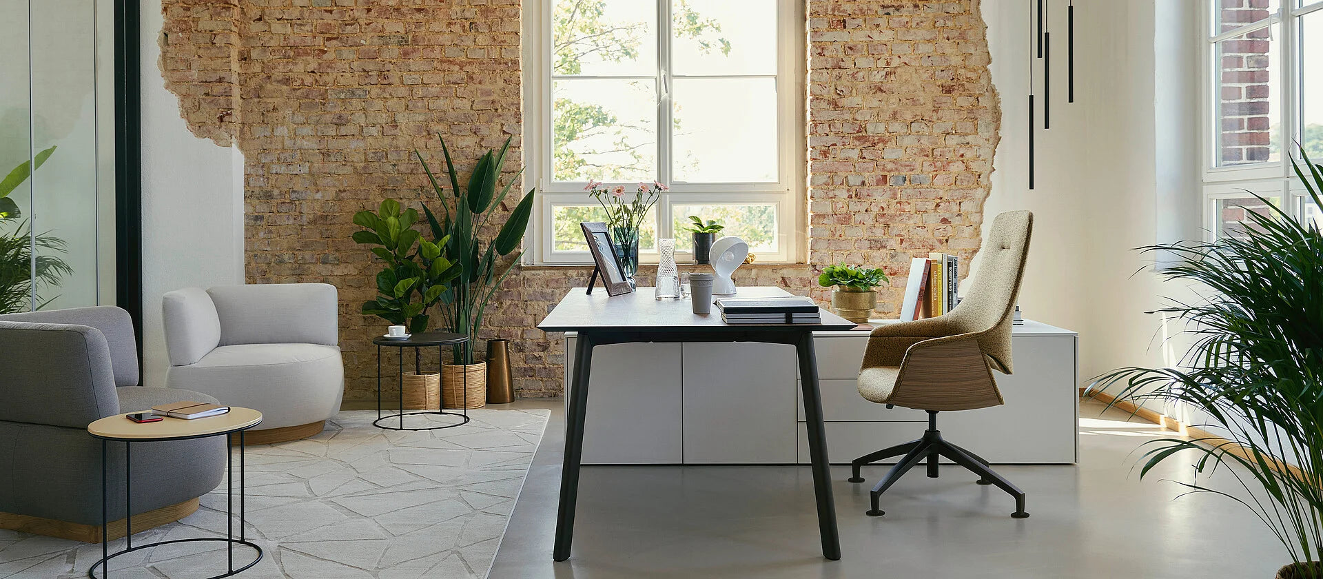 se:vision storage – Sideboard – Moderne Büroumgebung mit einem Tisch, einem bequemen Stuhl, Pflanzen und einer Backsteinwand im Hintergrund.
