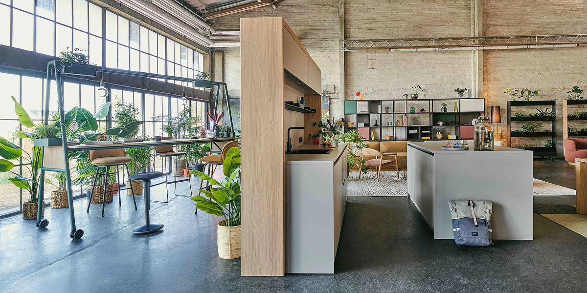 Bar se:café bar: Moderne Büroumgebung mit einem Holzregal und einer Küchenzeile in Grau. Pflanzen sorgen für eine angenehme Atmosphäre.