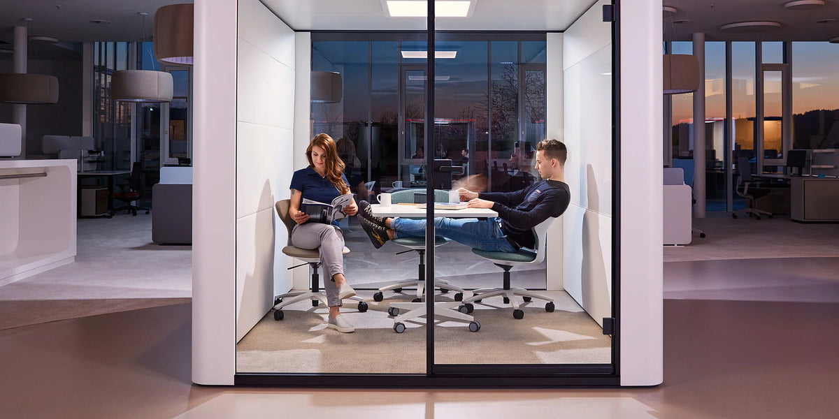 se:cube L – Meetingbox – Zwei Personen sitzen in einem geschlossenen Meetingraum mit Glaswänden auf Bürostühlen und lesen Unterlagen.