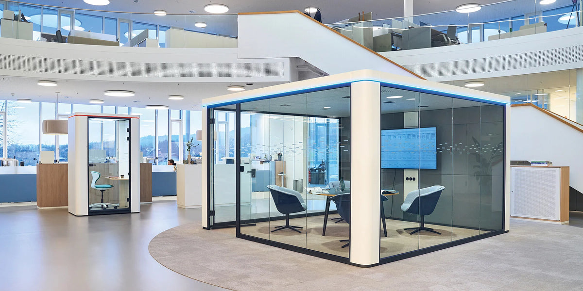 Meetingbox se:cube max: Moderne Büroräume mit Besprechungskabine aus Glas und Farbakzenten, helle Umgebung, stilvolle Möbel.