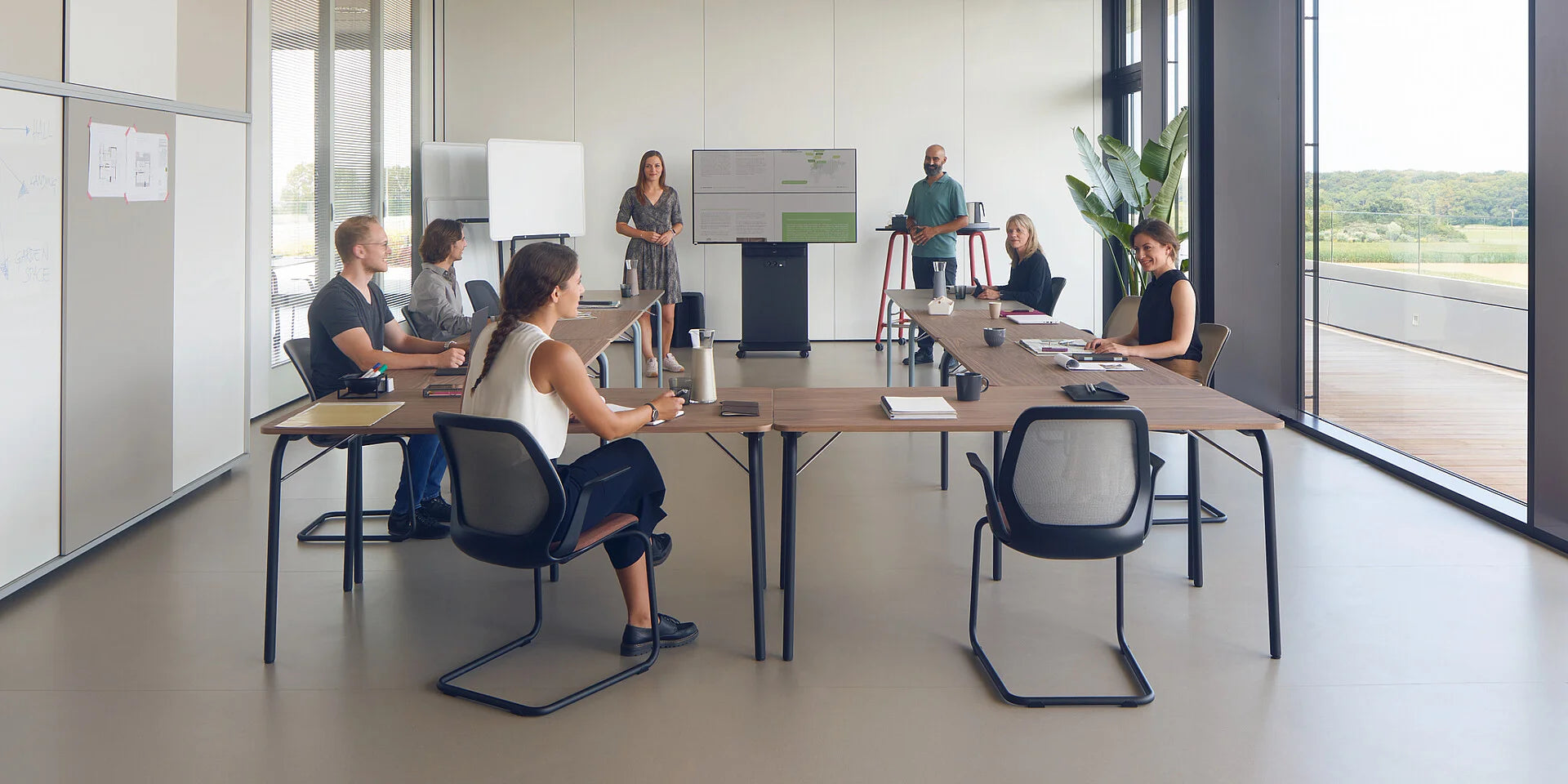 se:lab fold – Klapptisch – Ein Konferenzraum mit einem langen Tisch, mehreren Bürostühlen und einer Präsentationswand mit Monitor. Personen führen eine Besprechung.