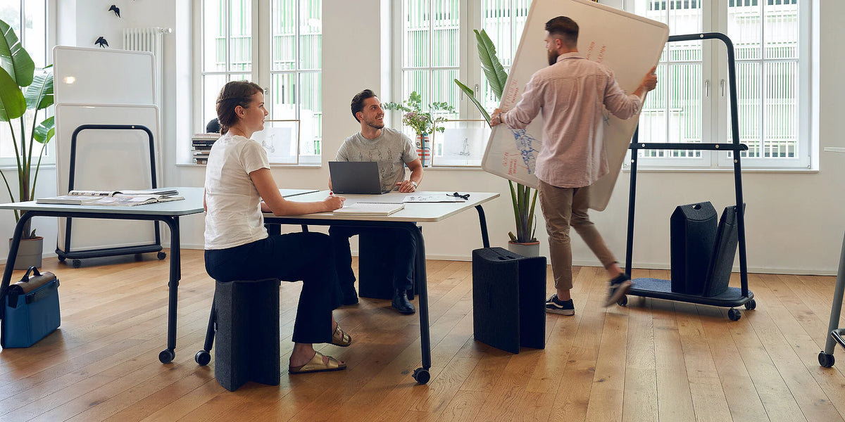se:lab work desk – Schreibtisch – Moderne Büroumgebung mit einem Tisch, Stühlen und einem mobilen Flipchart. Pflanzen im Hintergrund.