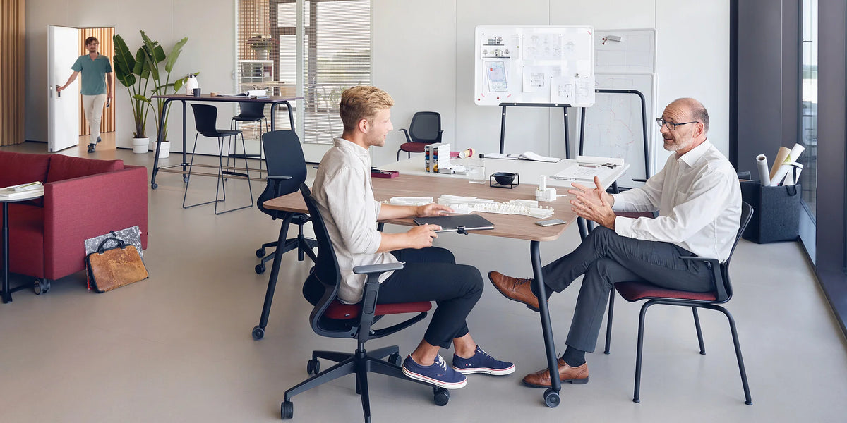 se:lab work desk – Schreibtisch – Modernes Büro mit Besprechungstisch, zwei Personen im Gespräch. Im Hintergrund ein Stehtisch und eine Wandtafel.