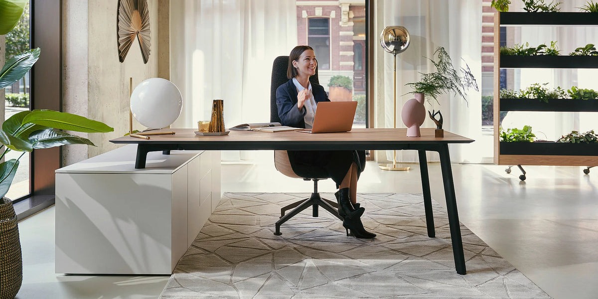 Schreibtisch mit Stauraum se:vision desk & storage: Ein moderner Schreibtisch aus Holz mit schwarzen Beinen, Laptop und Dekoration in einem hellen Büro mit Pflanzen.