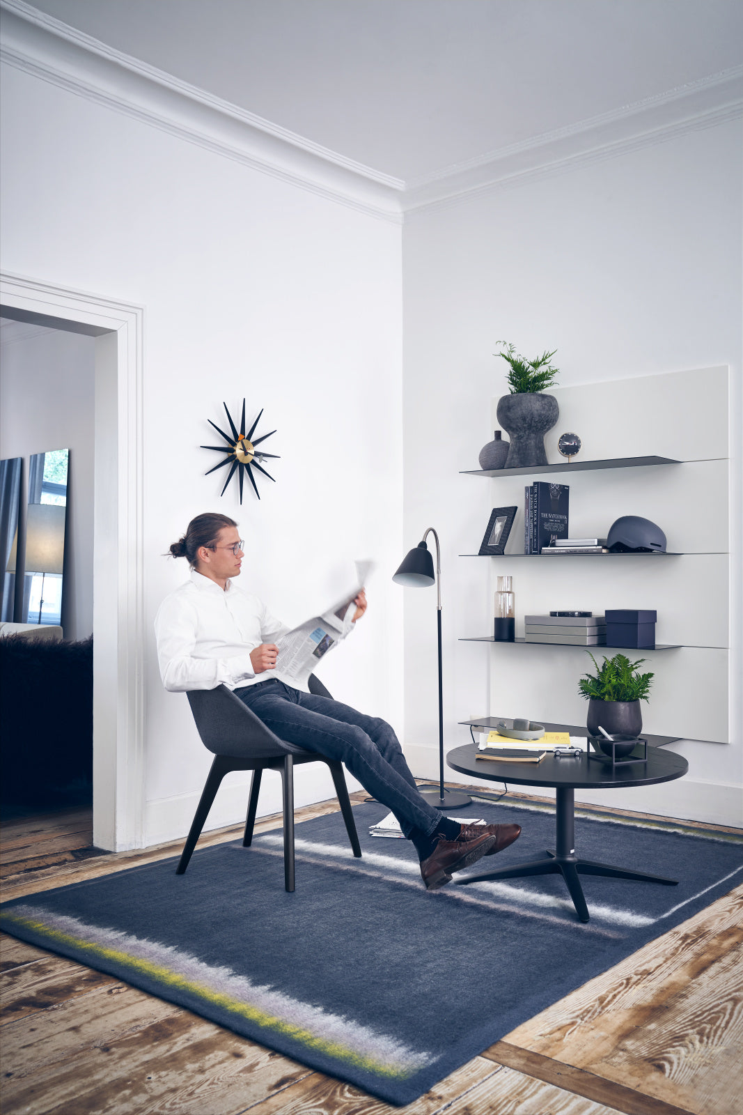 sweetspot – Lounge-Sessel – Person sitzt auf einem grauen Stuhl, hält eine Zeitung, neben einer schwarzen Tischplatte auf einem runden Tisch.