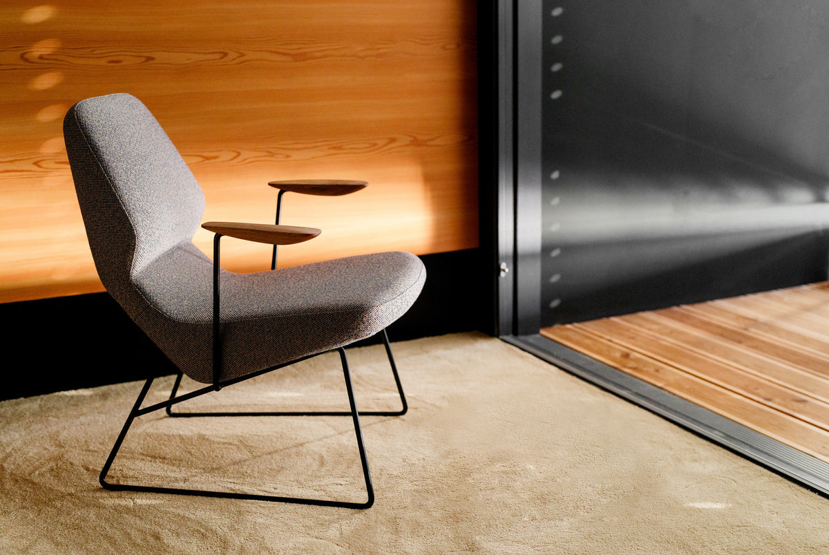 Oblique Loungesessel von Prostoria in Hellgrau mit Ablagetablett an einer Holzwand. © Prostoria