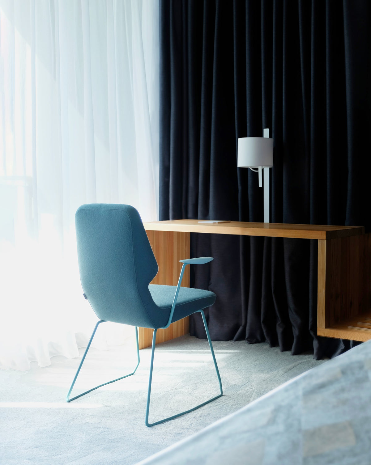 Oblique Stuhl von Prostoria in Blau an einem Schreibtisch vor dunklem Vorhang. © Prostoria