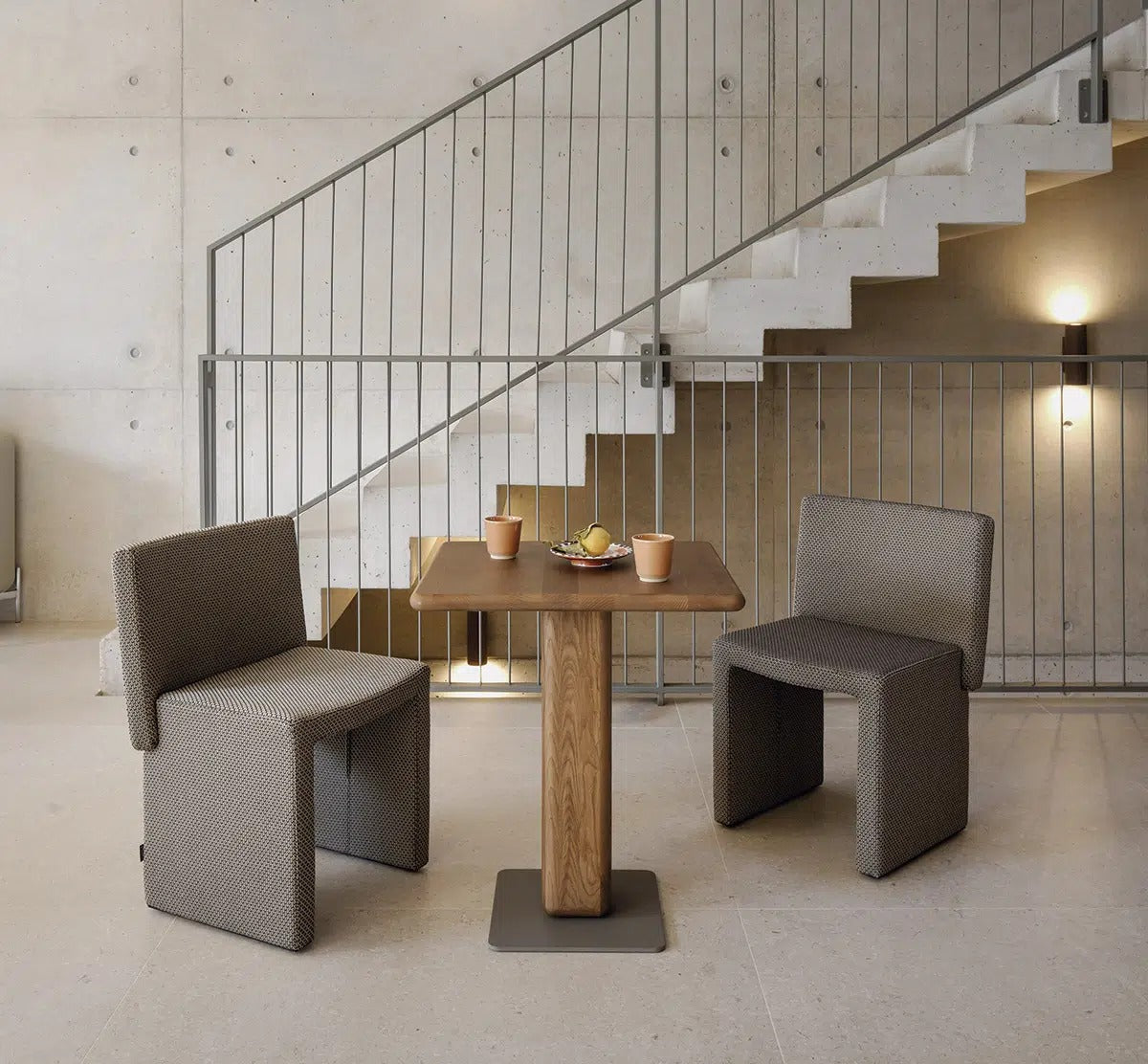 Zwei Sancal Cita Stühle in Grau an einem Cita Bistrotisch unter einer Betontreppe