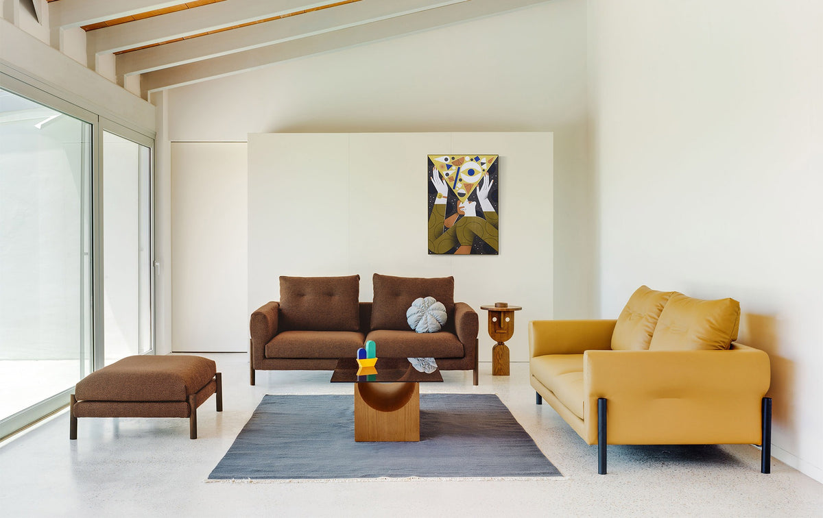 Sancal Momic Pouf in Dunkelbraun neben zwei Momic Sofas in einem hellen Wohnraum