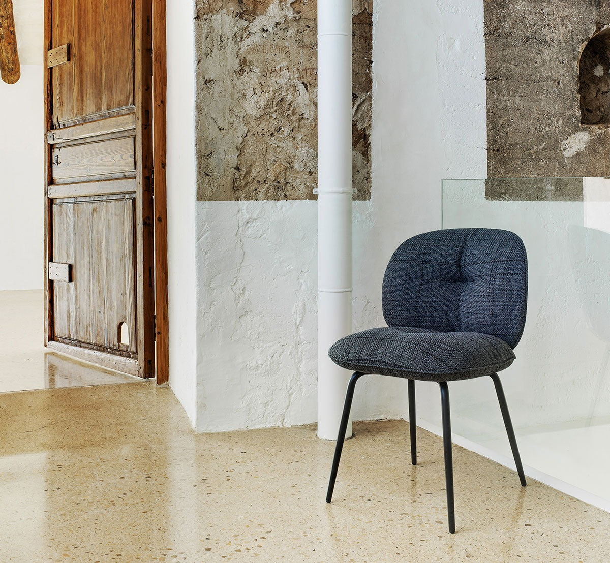 Sancal Mullit Stuhl in Dunkelblau mit schwarzen Metallbeinen neben einer alten Holztür