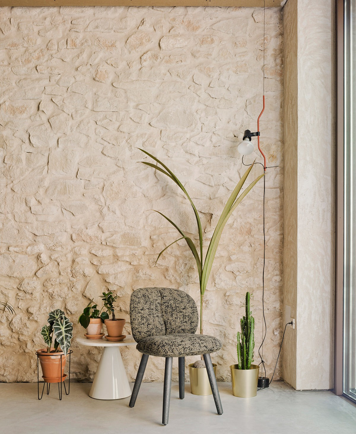 Sancal Mullit Stuhl mit gemustertem Bezug und Holzbeinen vor einer Natursteinwand