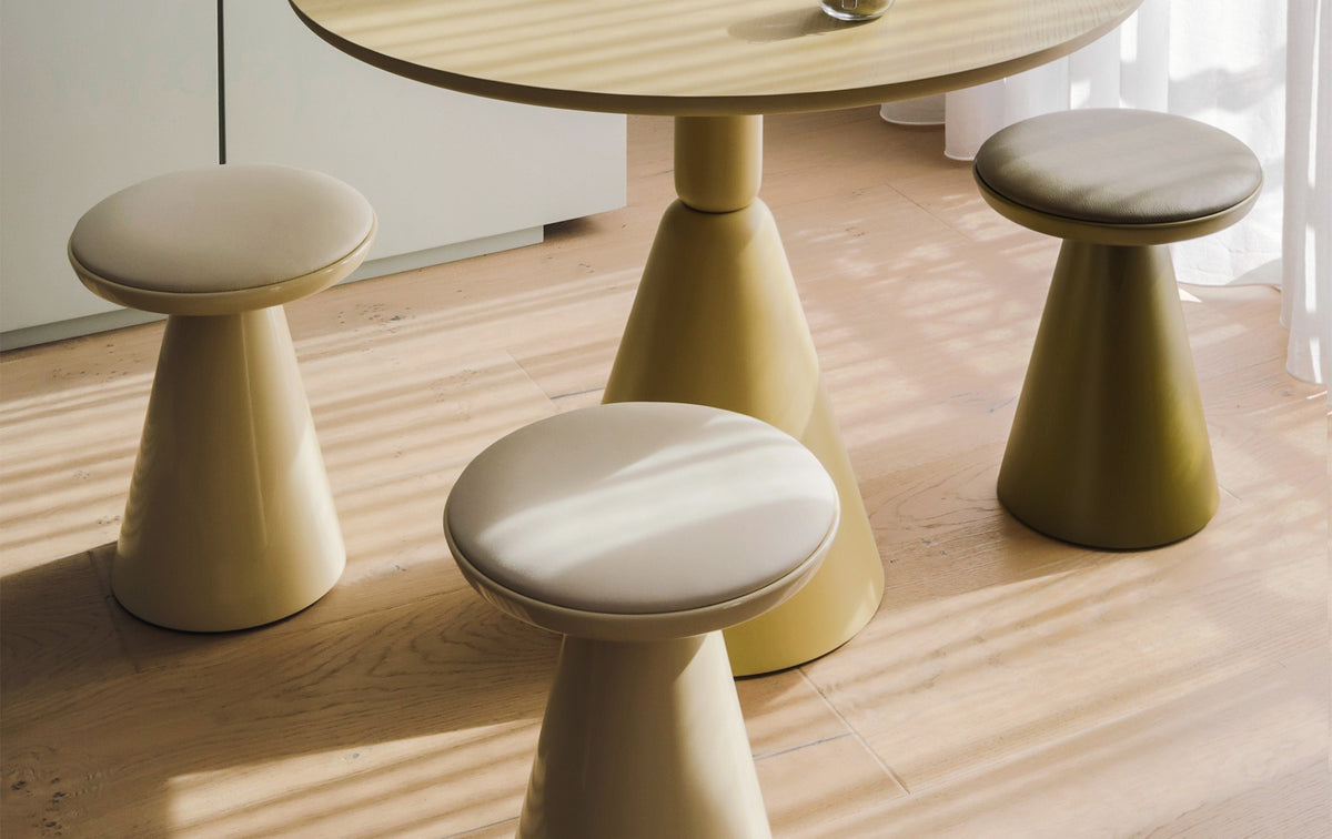 Drei Sancal Pion Hocker in Creme und Olivgrün um einen Pion Tisch im Sonnenlicht
