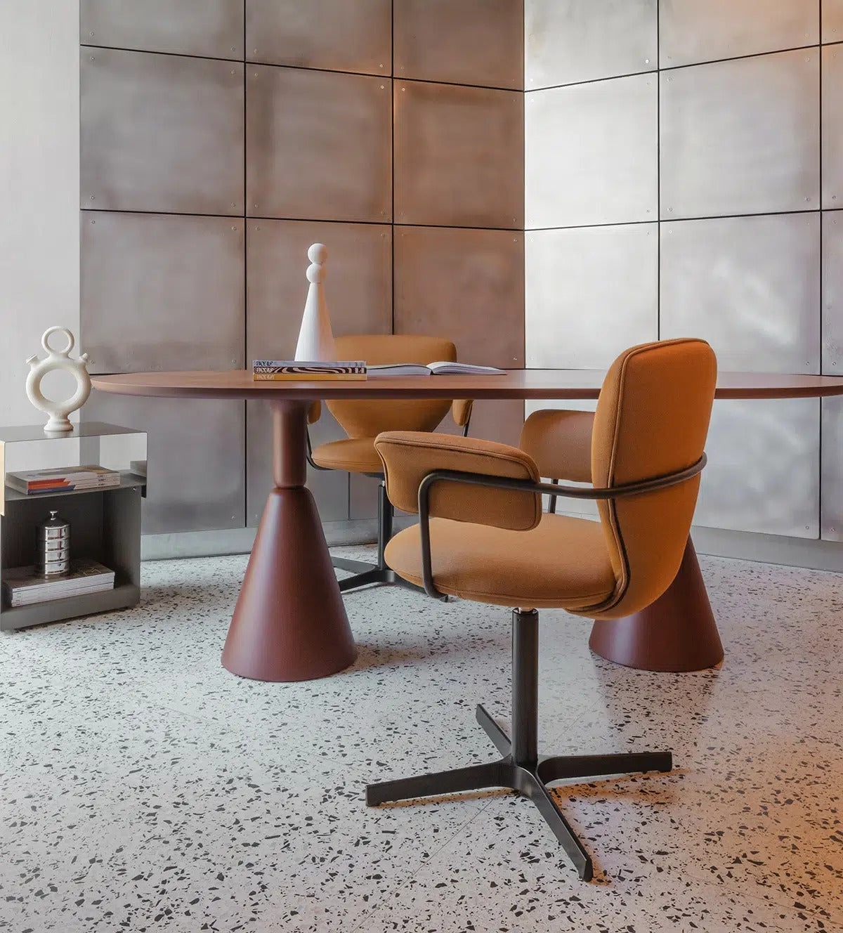 Sancal Planta Stuhl mit Armlehnen in Cognac auf Fusskreuz an einem runden Tisch vor einer Metallwand