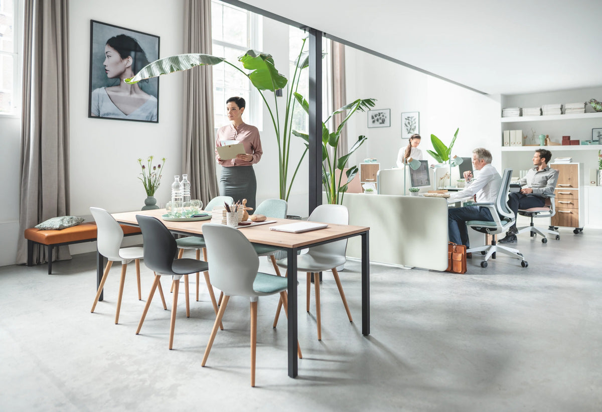 temptation four – Schreibtisch von Sedus – Tisch mit heller Platte in einem Büro mit Sesseln im Hintergrund.