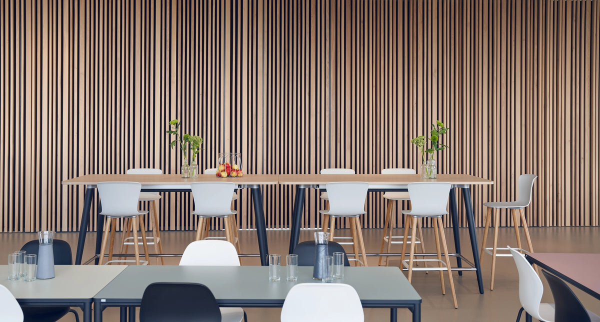 se:spot stool von Sedus mit Holzgestell an Hochtischen vor einer Lattenwand.