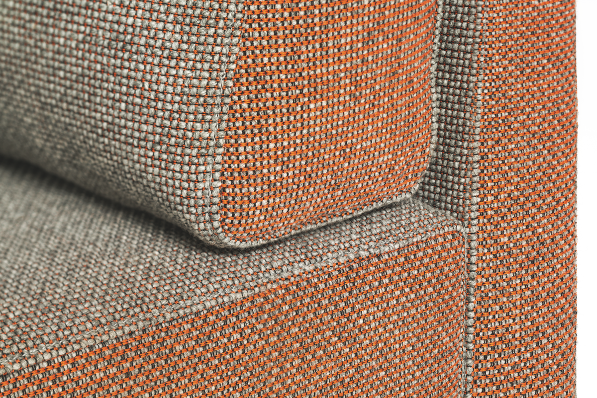 sopha – Sofa – Detailansicht eines grauen Sofas mit orangenem Gewebe an der Kante. Strukturierter Stoff, leicht gepolstert.